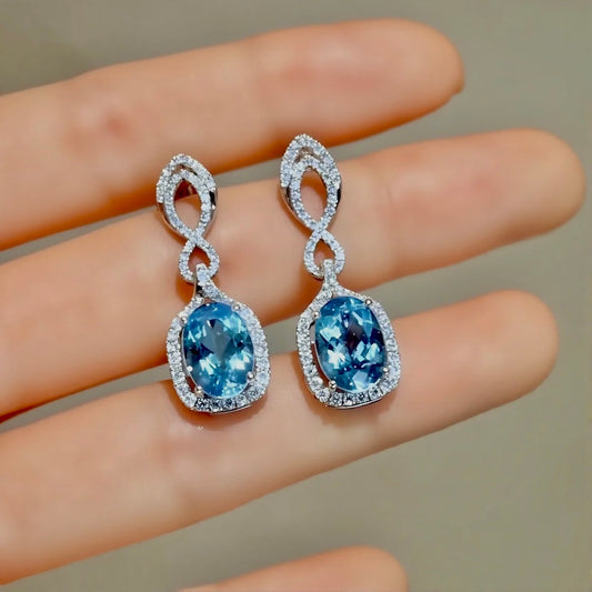 Oval aquamarine drop earrings with diamond halo and twisted white gold design
