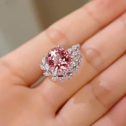 Floral-inspired ring with 4ct padparadscha sapphire in white gold setting surrounded by diamond leaves.