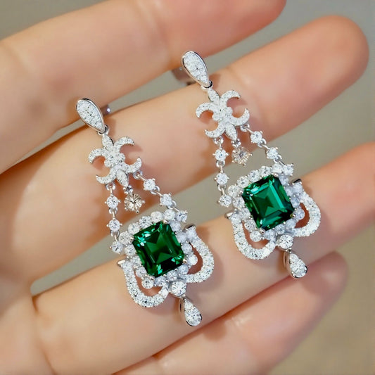 Ornate chandelier earrings with square emerald centers and diamond detailing in white gold
