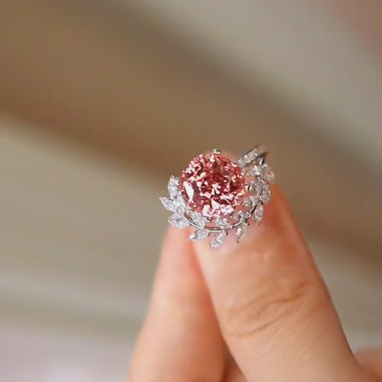 Floral-inspired ring with 4ct padparadscha sapphire in white gold setting surrounded by diamond leaves.